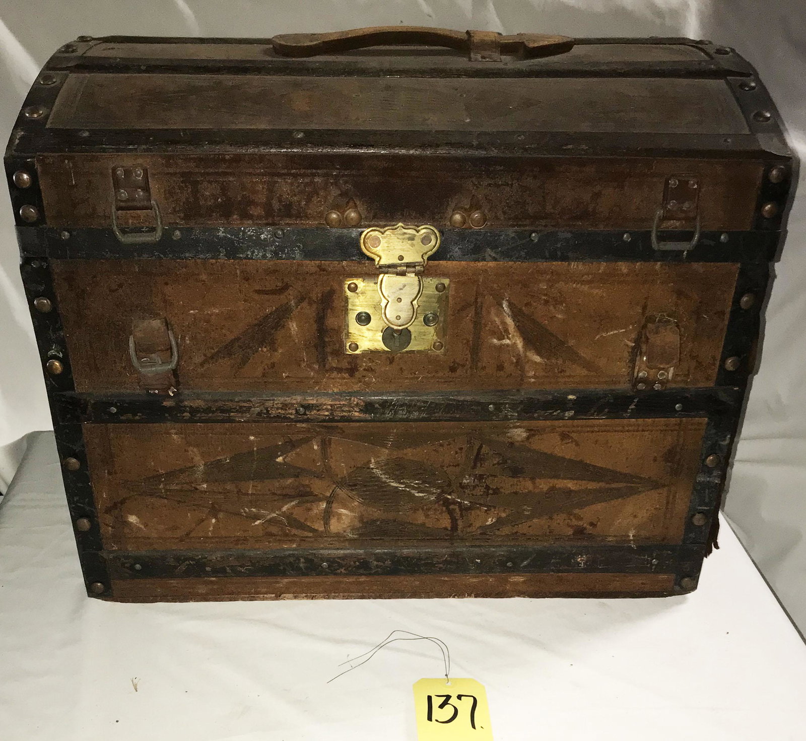 Small Dome Top Trunk: Small antique dome top trunk w/brass latch and key, original tooled leather covering w/wood staves, metal mounts and rivets, covering worn and faded, torn on sides and back, leather arrow form handle 