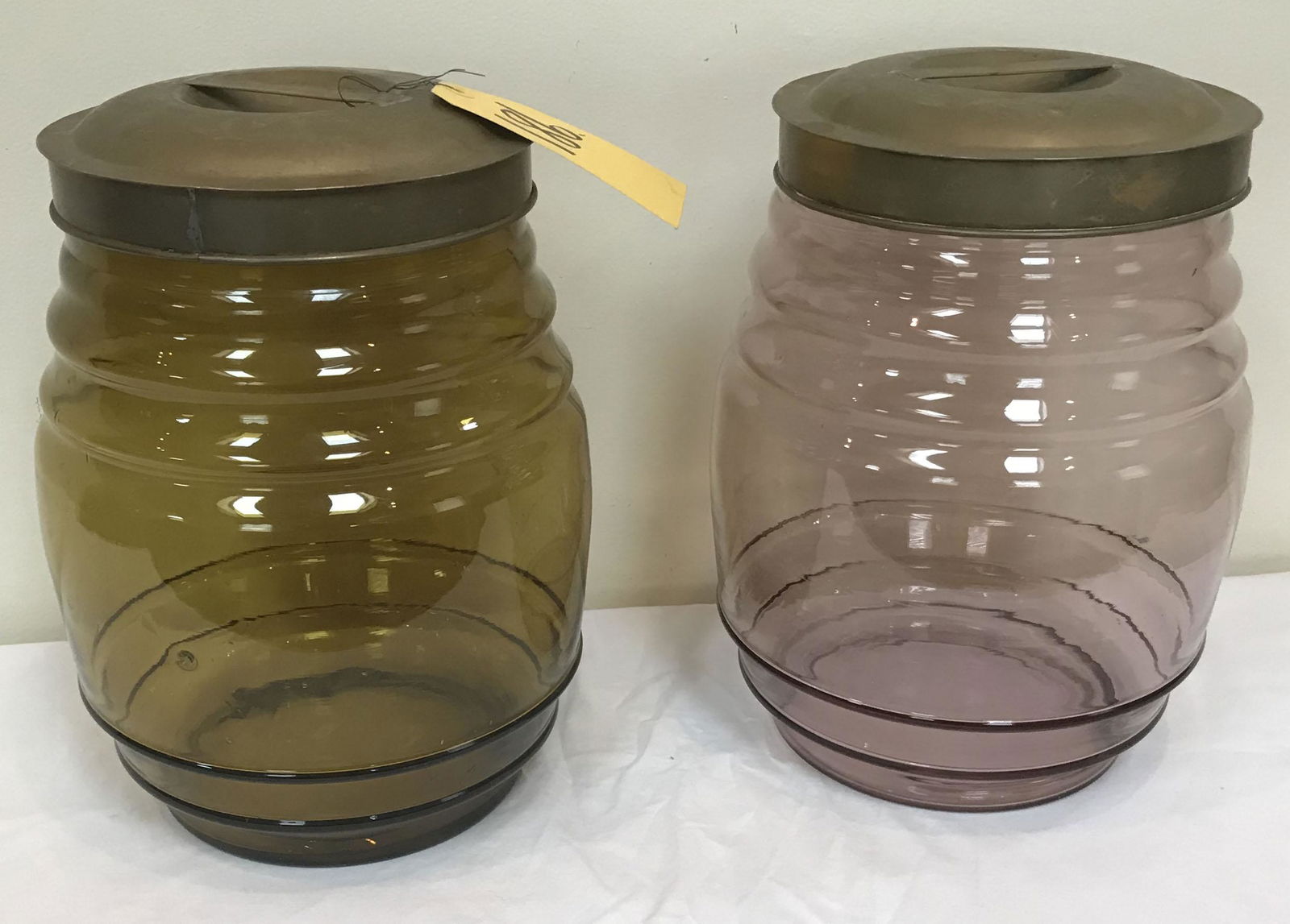 Pair Glass Store Jars: Pair of later barrel form glass store jars both w/brass lids: (1) w/greenish tint, visble straw marks side and base-NOT cracks, interior rim shows several chips, approx. 13 3/4" T x 9" diameter; AND a