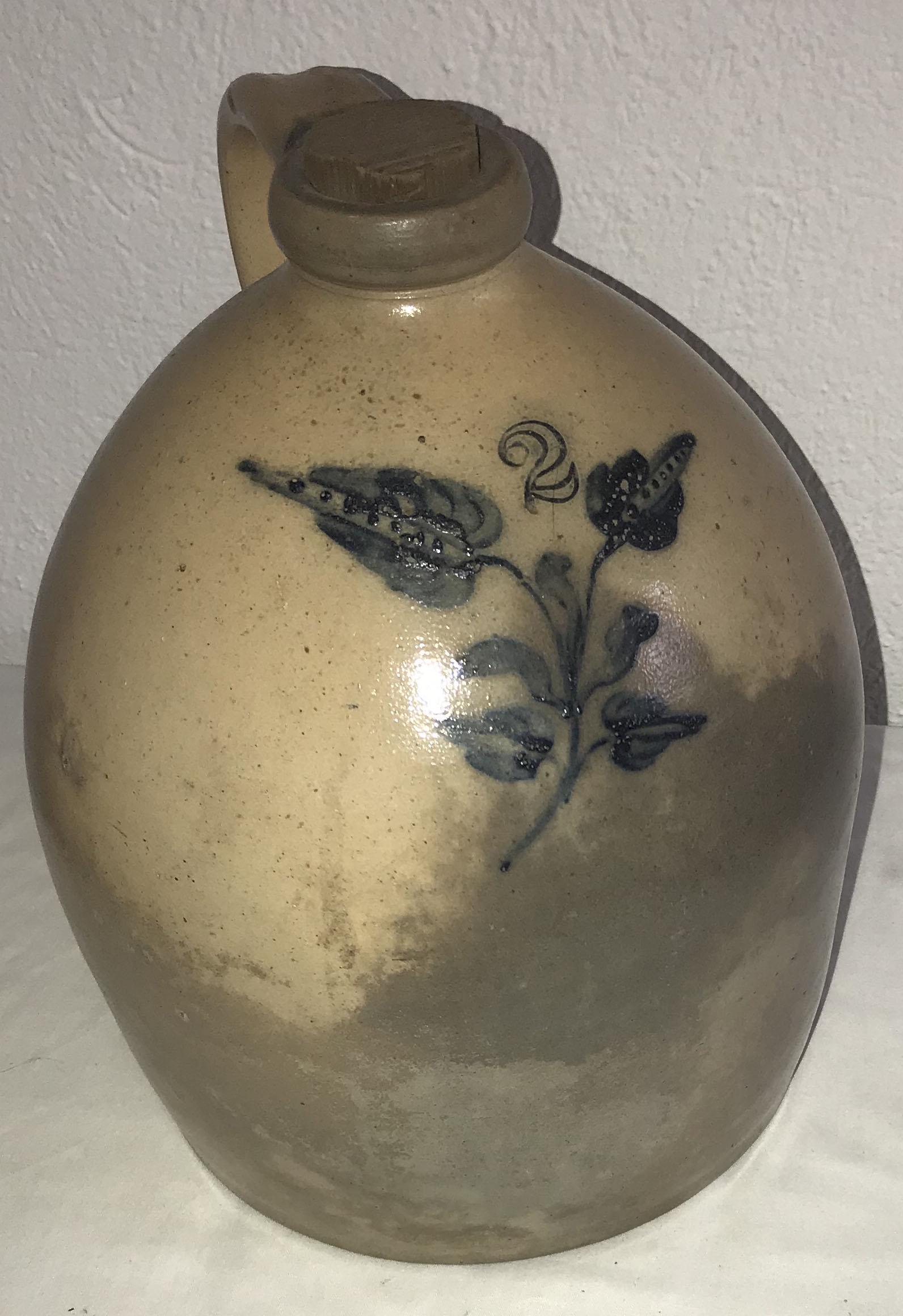 Blue Decorated Stoneware Jug: 19th century blue decorated 2 gallon stoneware jug, leaf and stem design, chip on top of handle, minor rim chip, old surface and old discoloration visible, wooden plug, 20" T x approx. 9" base diamete