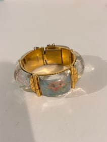 vintage gold-tone hinged bangle bracelet with a clear resin or lucite inlay containing a floral