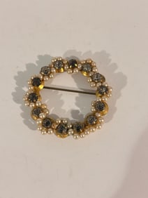 This is a vintage glass rhinestone circle wreath brooch pin with faux pearls and green-toned