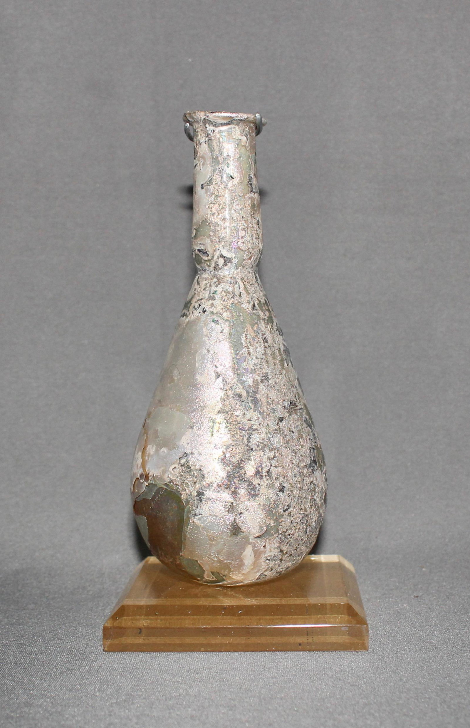 Roman Golden Iridescent Unguentarium: Roman, circa 1st-2nd century AD. This gold colored unguentarium (a vessel likely used for oils) has areas of beautiful iridescence. This piece comes on a custom plexiglass base. Ex. Private American c