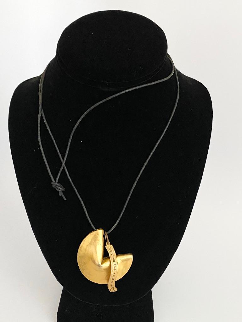 A VINTAGE 70'S GOLD PLATED FORTUNE COOKIE WITH CHARM: A fun solid gold plated fortune cookie with "paper" plated metal charm fortune that reads "Cupid Aims Your Way" On an original adjustable leather cord that is currently tied to 32". The cookie measure