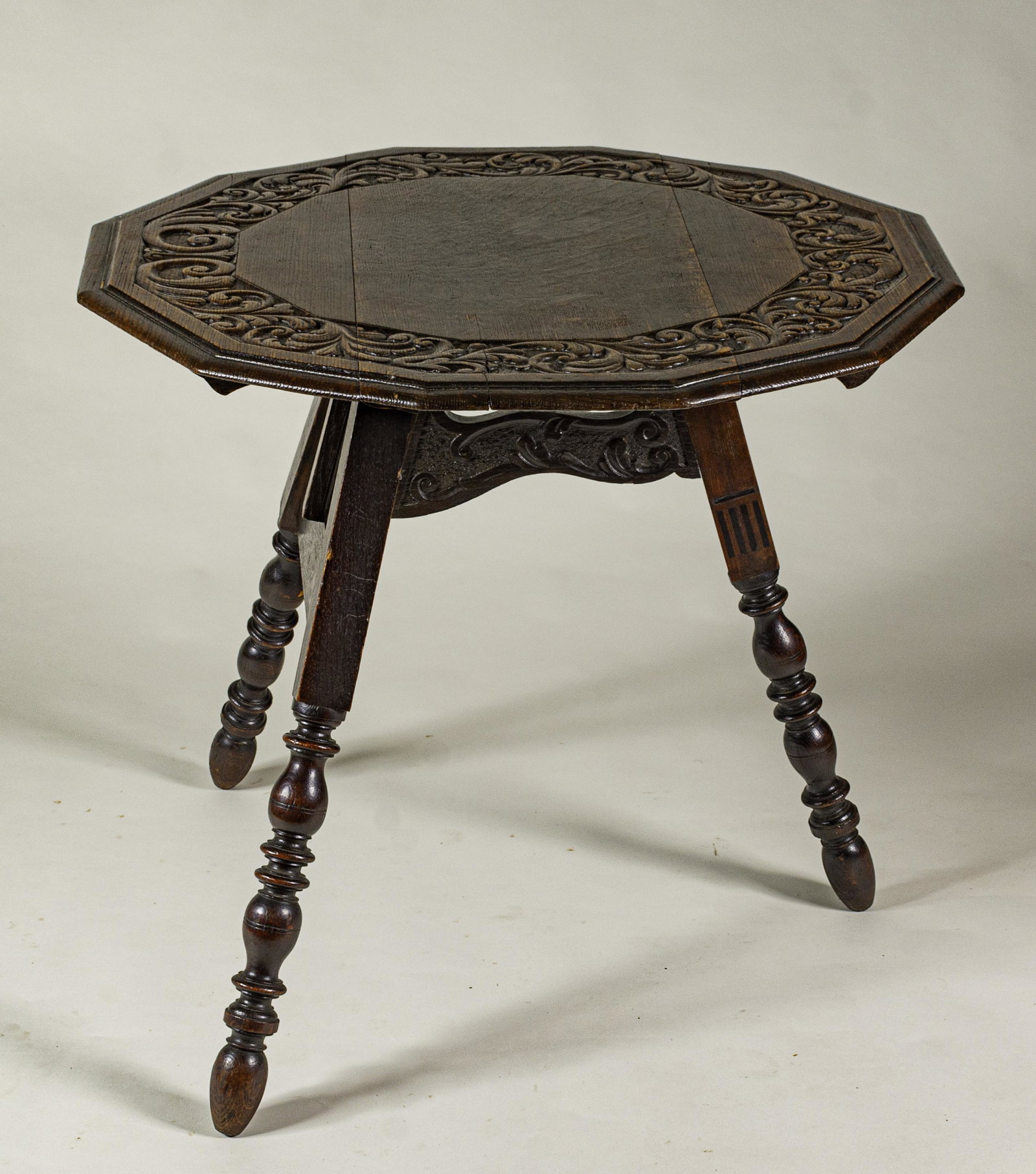 Jacobean Carved Oak Folding Table: Circa 1900. With carved, turned and inlaid base and folding leg mechanism, 12-sided top with deeply carved border, 26.75 x 31.75"