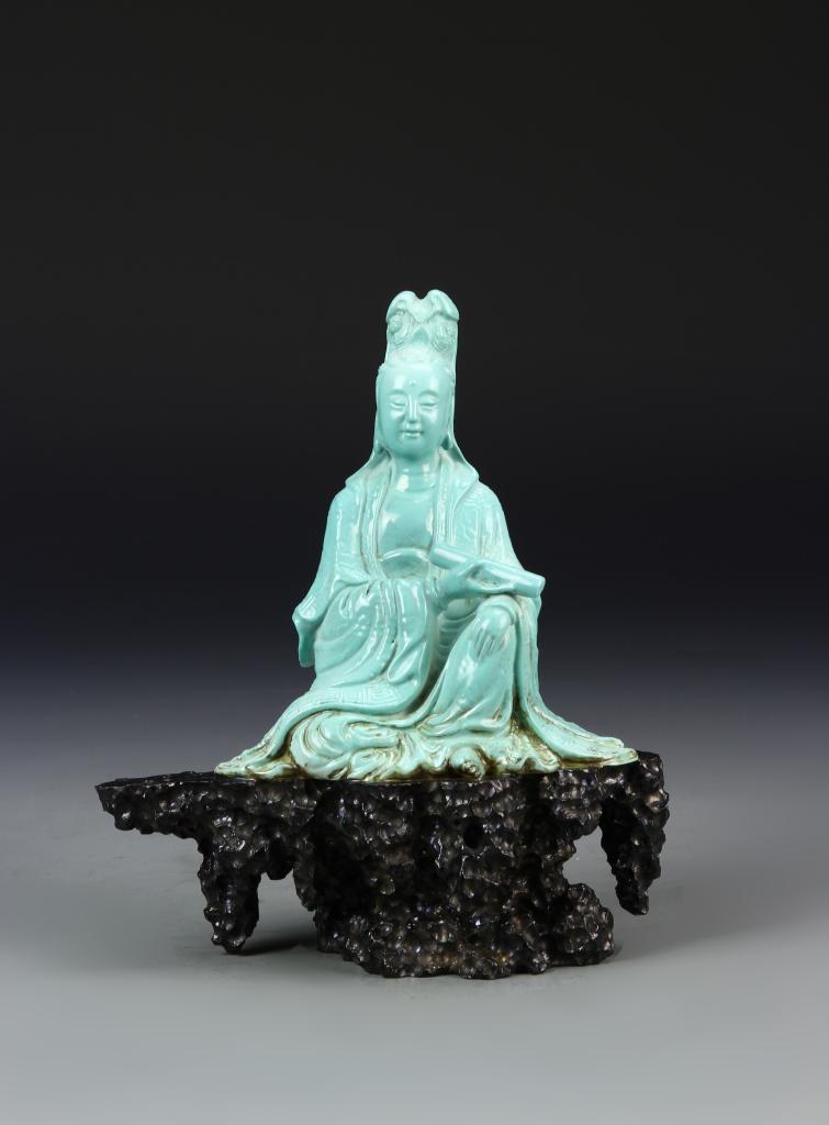 Chinese Porcelain Guanyin: China, 19th C., porcelain Guanyin, seated in flowing robes, wearing a high headdress and holding a scroll with one hand leaning on one knee, imitation turquoise stone and placed on a densely carved wo