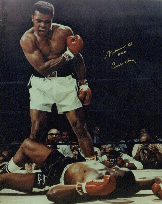 MUHAMMAD ALI - Large Liston Fight Photo Signed: Muhammad Ali. 16" x 20" color photograph of Ali standing over Sonny Liston, signed in gold ink "Muhammad Ali A. K. A. Cassius Clay." The photograph is double matted and framed to 22" x 26".