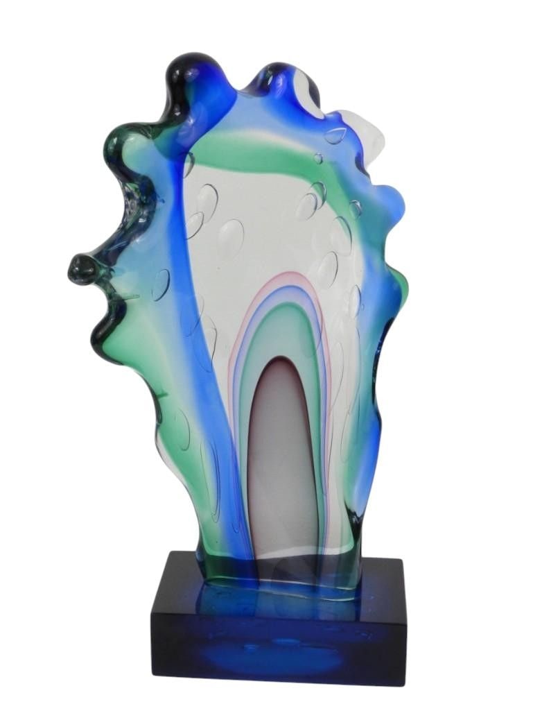 Abstract Art Glass Sculpture with Blue, Green, Pi: This abstract art glass sculpture features a dynamic composition of flowing colors, primarily in shades of blue and green, accented with subtle pink and white elements. The piece is characterized by i