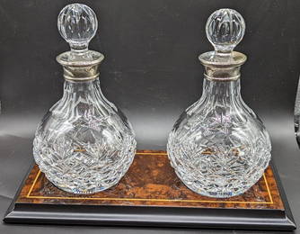 A pair of Mapping and Webb silver collared glass decanters on burr walnut veneered base, with