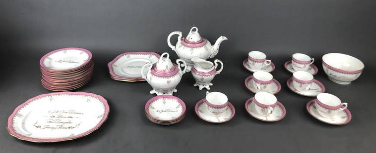 19th Century White, Pink, & Gilt Partial Dish Set: Inscribed to Mrs Jane Deacon from her daughter Jenny Homes. Comprising of teapot, creamer, sugar, 3 serving dishes, 12 plates, bowl , 7 cups and saucers, and 4 spare saucers.