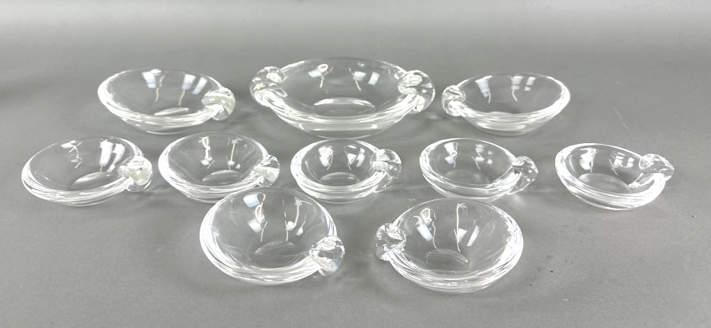 Group of 10 Steuben Nut Bowls / Ashtrays: Group of 10 Steuben Nut Bowls / Ashtrays. Largest: 2 1/4"h x 81/2"w x 7"d. Condition: Some scuffs on bottom of bases, largest bowl with a fracture by handle.