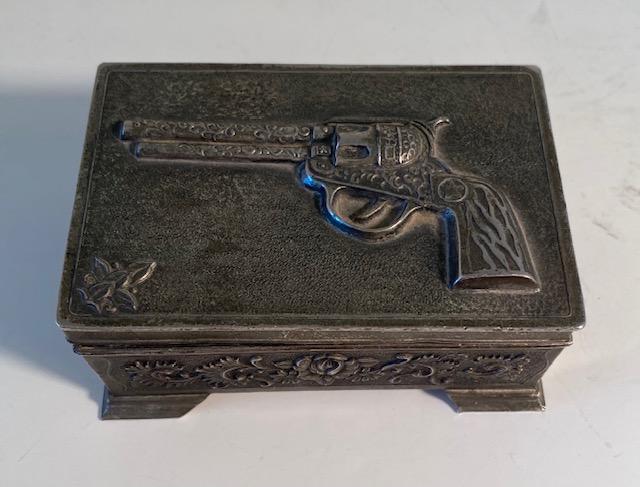 Metal Trinket Box with Cowboy Motif: Metal trinket box with cowboy/gun motif. Top inside is missing the felt and has been ball point pen marked. Box measures 4" x 2.75" x 1.75"