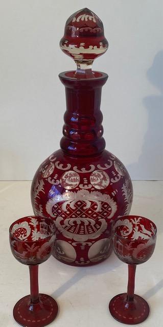 Bohemian Ruby Red Wine Decanter and 2 Glasses: Bohemian ruby red wine decanter with two glasses. Glasses are stemmed and measure 4 inches by 1 3/4 inches. Decanter measures 12 inches high by 3.5 inches wide at the base. Some slight wear on the red