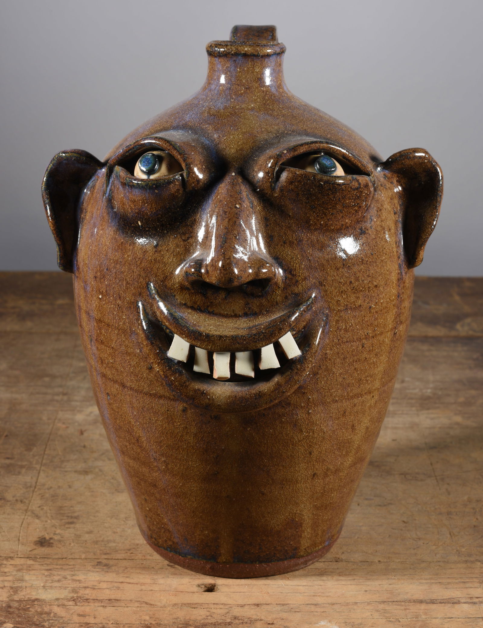 Don Craig Face Jug: 11" smiling face jug by Don Craig. Sinle row of broken china teeth with clay eyes. Signed on bottom.
