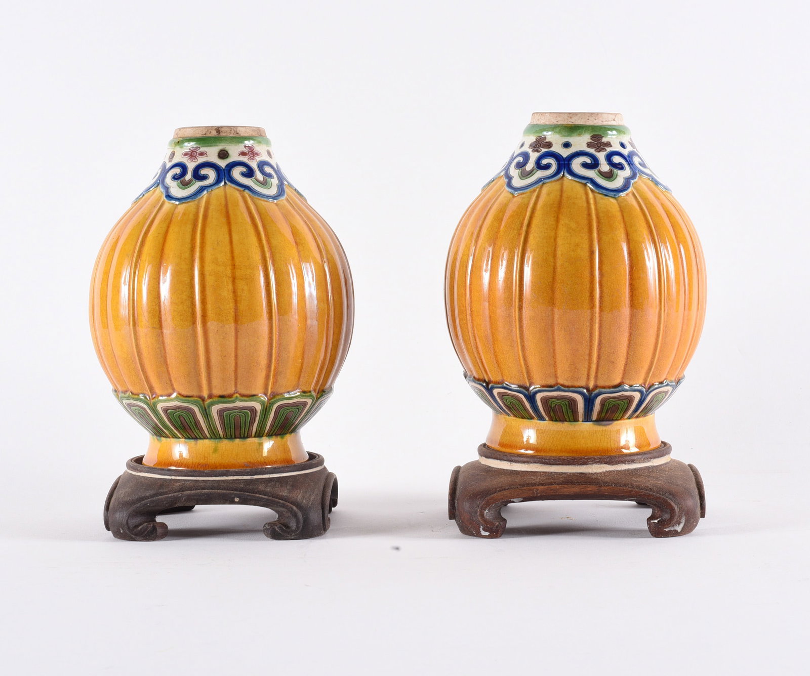Pair Chinese Sancai-Style Glazed Porcelain Jars on Wooden Stands: 8" Decorative pair of ribbed porcelain jars featuring vibrant sancai-style glazing in amber, green, and cobalt tones. Each of globular form with fluted body and stylized border motifs at neck and foot