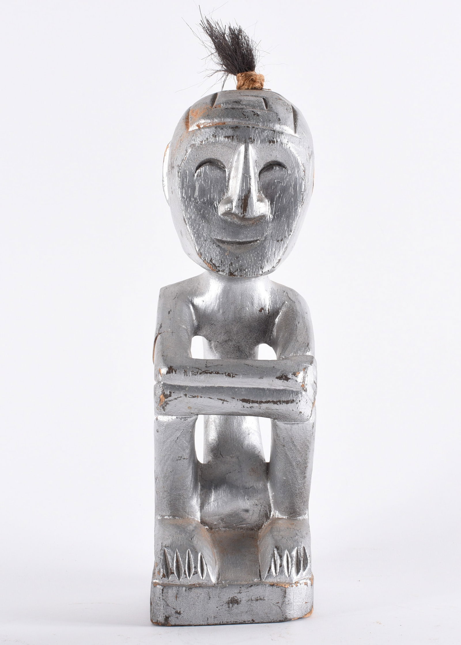 African Carved Wooden Figure with Metallic Finish: 12" Hand-carved wooden figure depicting a seated stylized human form with elongated features, finished in metallic silver paint. Likely African in origin, possibly mid to late 20th century decorative 