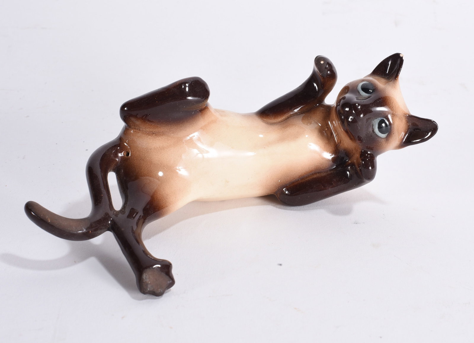 Vintage Glazed Ceramic Siamese Cat Figurine: Mid-century style ceramic Siamese cat figurine with glossy brown and cream glaze, modeled in a reclining pose with expressive eyes.