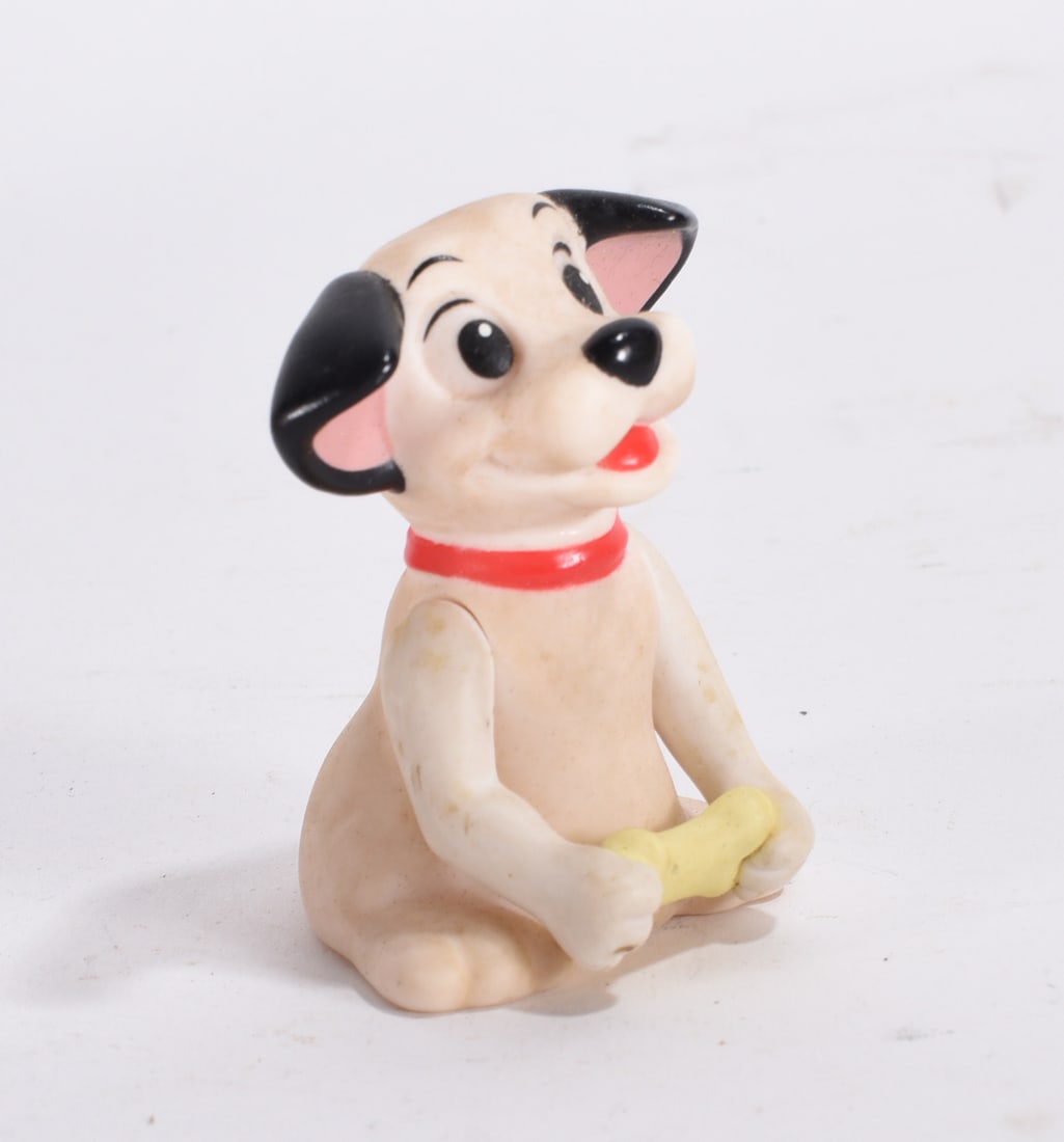 Cartoon Style Puppy Figurine: Cartoon style ceramic puppy figurine seated holding a yellow bone with painted red collar.