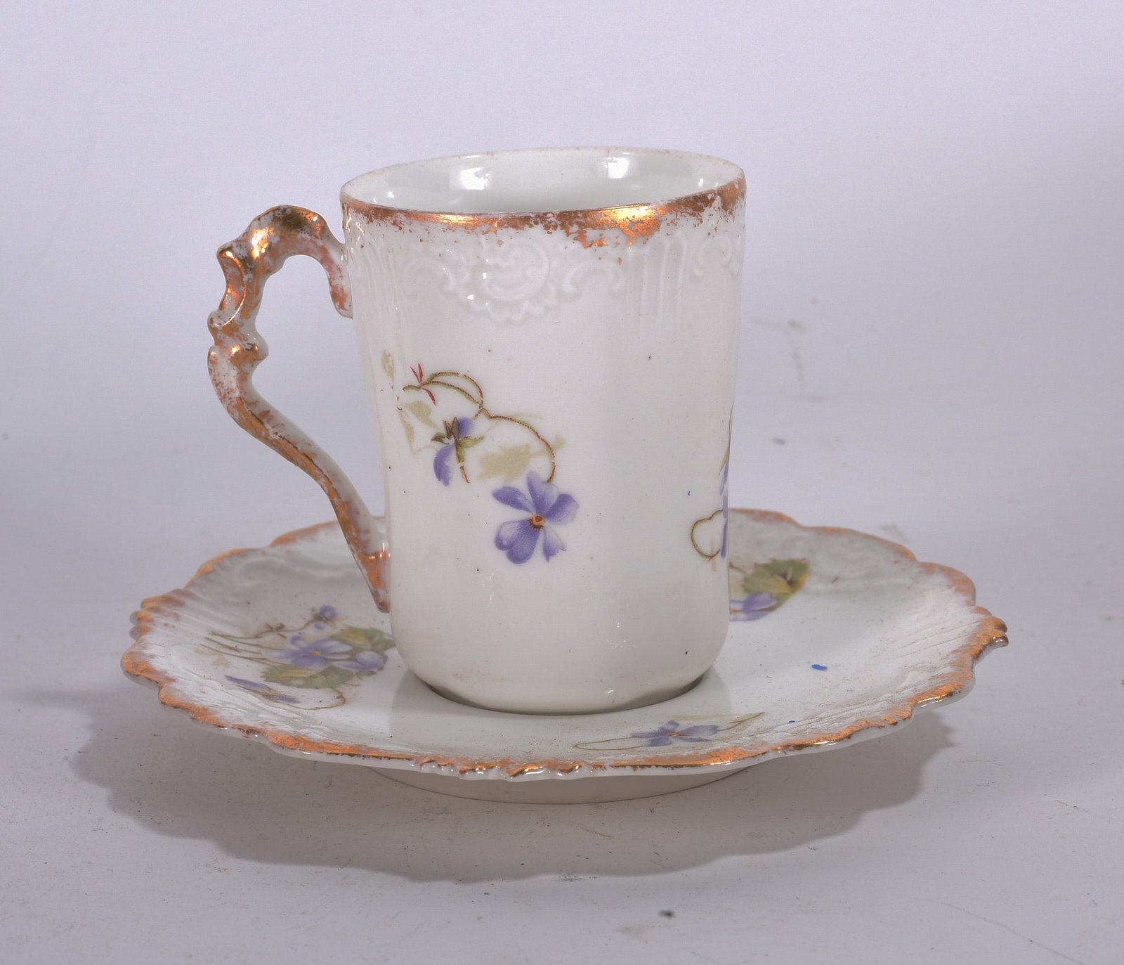 Floral Porcelain Cup and Saucer: White porcelain cup and saucer with purple floral decoration and gold trim.