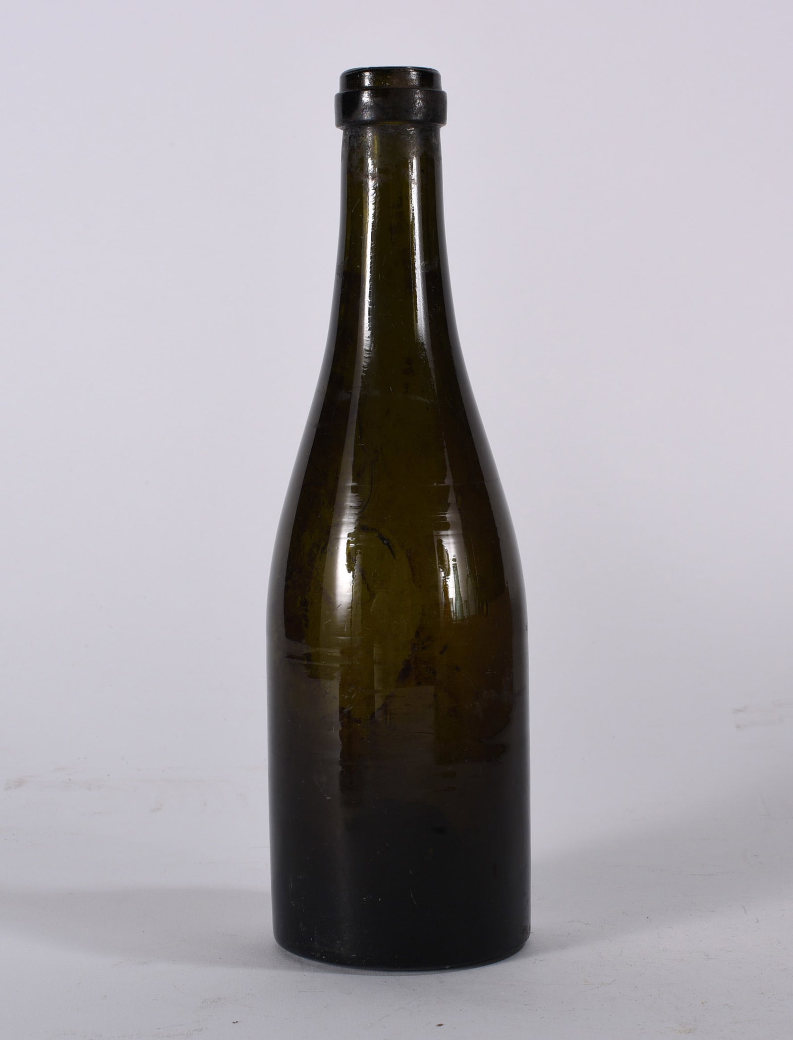 Dark Olive Wine Bottle: Antique dark olive green wine bottle with tapered neck and rounded shoulder. Surface scratches and age wear visible throughout.