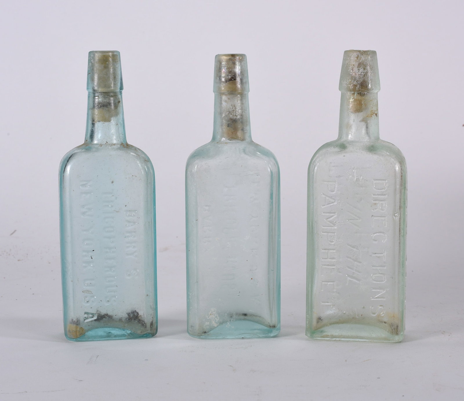 Antique Bottles: Group of embossed antique medicine bottles including paneled and cylindrical examples with varying aqua tones and surface wear.