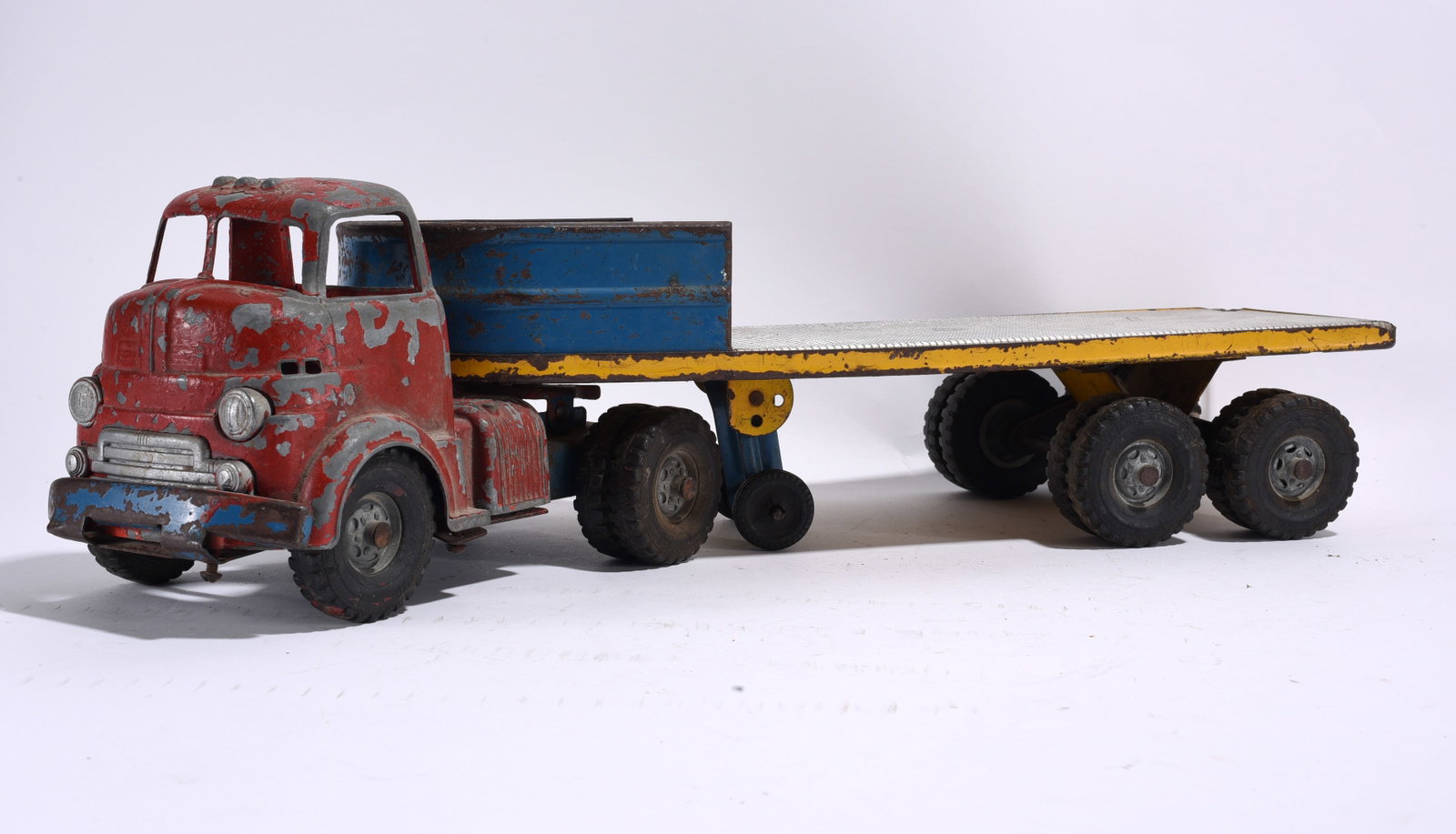 Pressed Steel Flatbed Semi Truck with Trailer: Vintage pressed steel flatbed semi truck with detachable trailer. Red and blue paint scheme with heavy play wear, paint loss, and oxidation throughout.