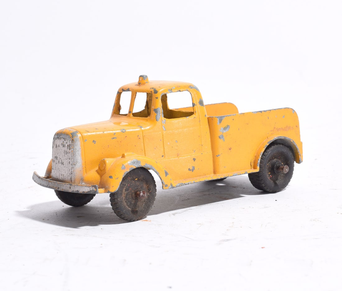 Cast Metal Pickup Truck: Cast metal pickup truck finished in yellow paint with silver-toned grille and bumper. Features black wheels and open cargo bed. Paint wear, oxidation, and age-related surface losses evident.