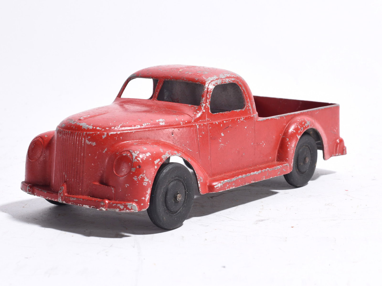 Pressed Steel Pickup Truck: Pressed steel pickup truck with red painted body and black wheels. Features rounded cab styling and open cargo bed. Moderate paint wear and surface scratches throughout.