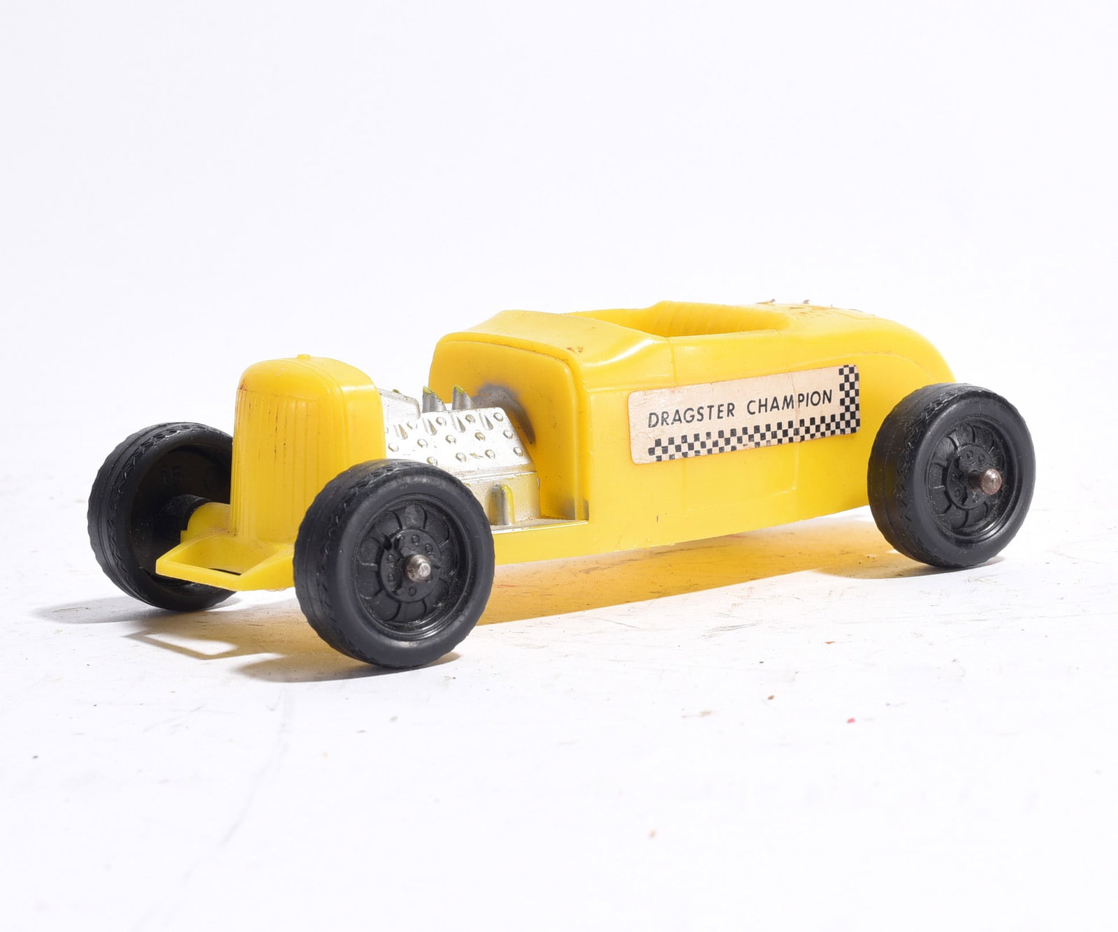 Dragster Champion Racing Car: "Dragster Champion" racing car in yellow plastic with exposed silver-toned engine detail and original side decal. Open cockpit design with black wheels. Minor wear consistent with age and use.