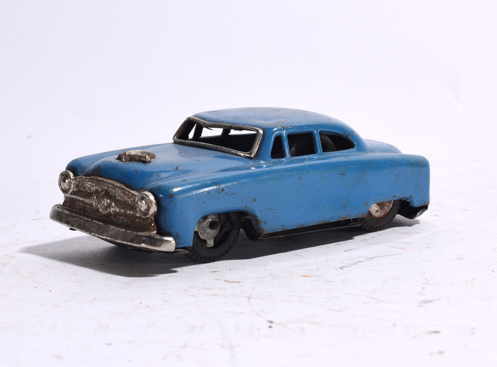 Blue Tin Sedan Automobile: Blue pressed steel sedan automobile featuring chrome-style grille and bumper details. Shows scattered paint wear, oxidation, and age-related surface marks.