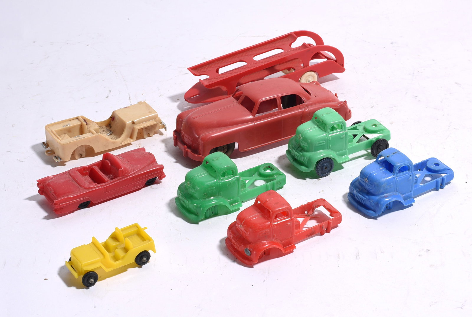 Group of Nine Assorted Plastic Toy Vehicles and Parts: Group lot of nine assorted plastic toy vehicles and parts including tow trucks, convertible, sedan, jeep, and trailer components. Various colors and conditions with scattered wear and missing pieces.