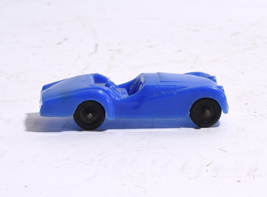 Blue Plastic Open Top Sports Car: Blue molded plastic open-top sports car with streamlined body and rolling wheels. Light surface wear and age-related handling marks noted.