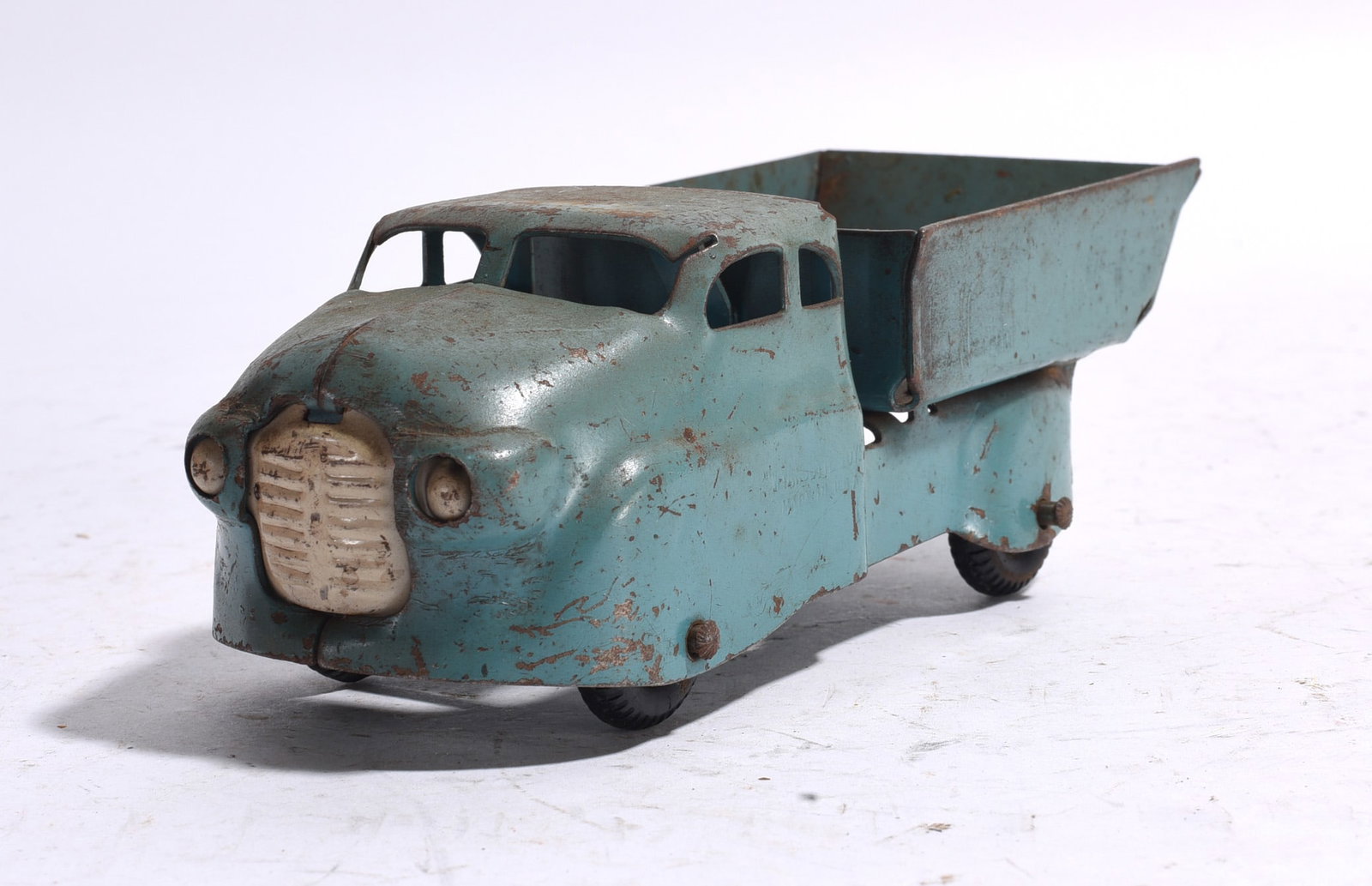 Vintage Pressed Steel Dump Truck: Vintage pressed steel dump truck with light blue-green finish and tilting dump bed. Three-wheel configuration with lithographed grille details. Showing paint wear, oxidation, and evidence of long-term