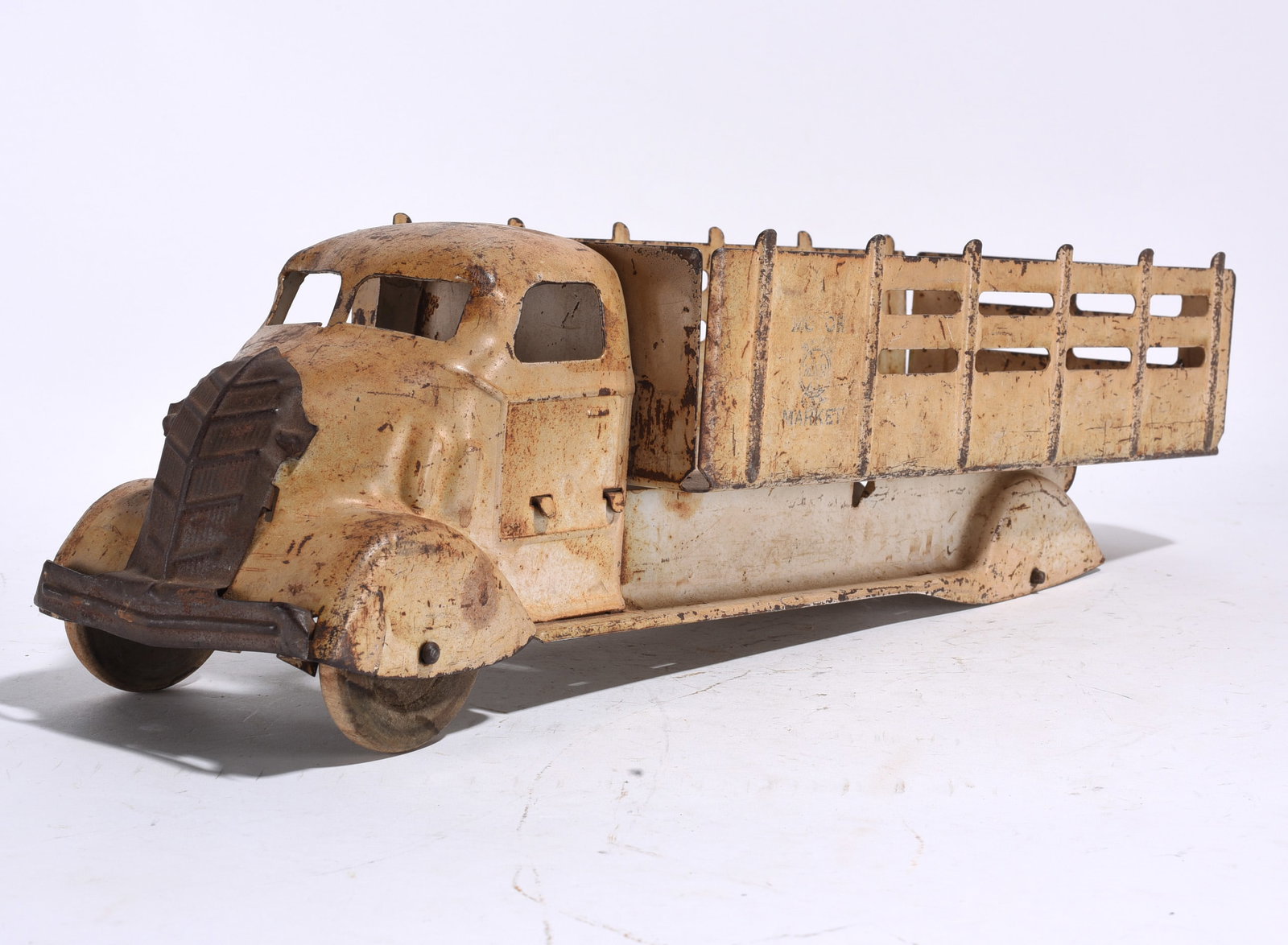 Vintage Pressed Steel Stake Bed Truck: Early pressed steel stake bed truck with cream painted finish and black grille. Retains partial side graphics and original wheels. Surface wear and oxidation throughout.