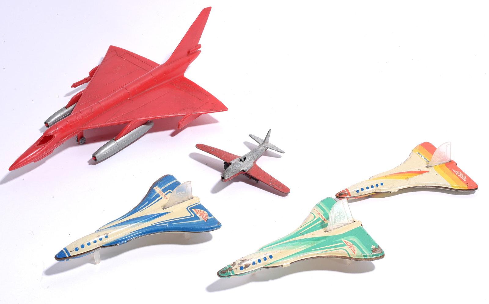 Assorted Toy Airplanes and Supersonic Jets Group: Group of vintage toy aircraft including a large red plastic jet fighter, die-cast airplane, and three lithographed friction-style supersonic jet toys. Showing play wear and surface marks from use.