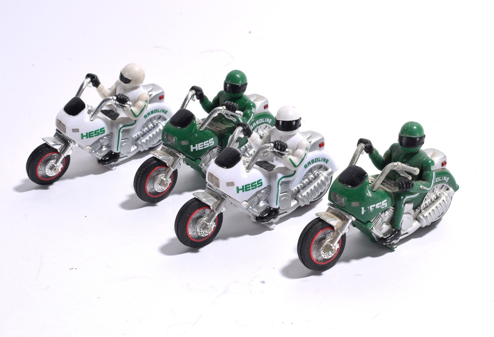 Hess Motorcycle Toy Group: Group of four Hess toy motorcycles with rider figures, including green and white examples. Detailed miniature promotional toys with light handling wear.