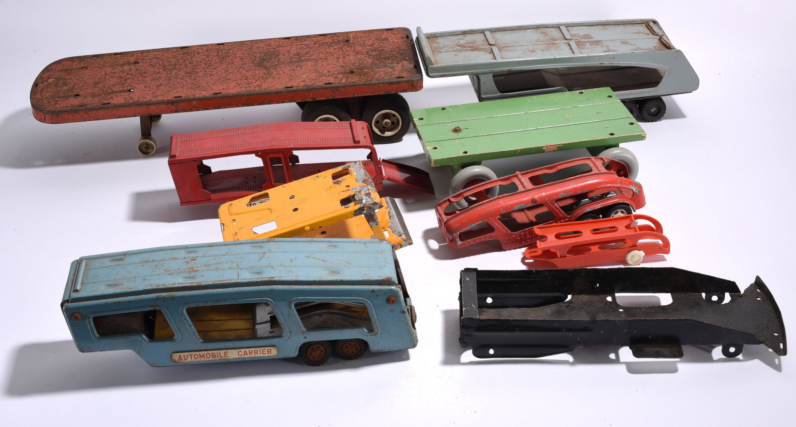 Assorted Toy Transporters and Trailer Parts: Assorted pressed steel and metal toy transporters, trailers, automobile carriers, sleds, and vehicle body components. Surface wear, oxidation, and paint loss consistent with age and use.
