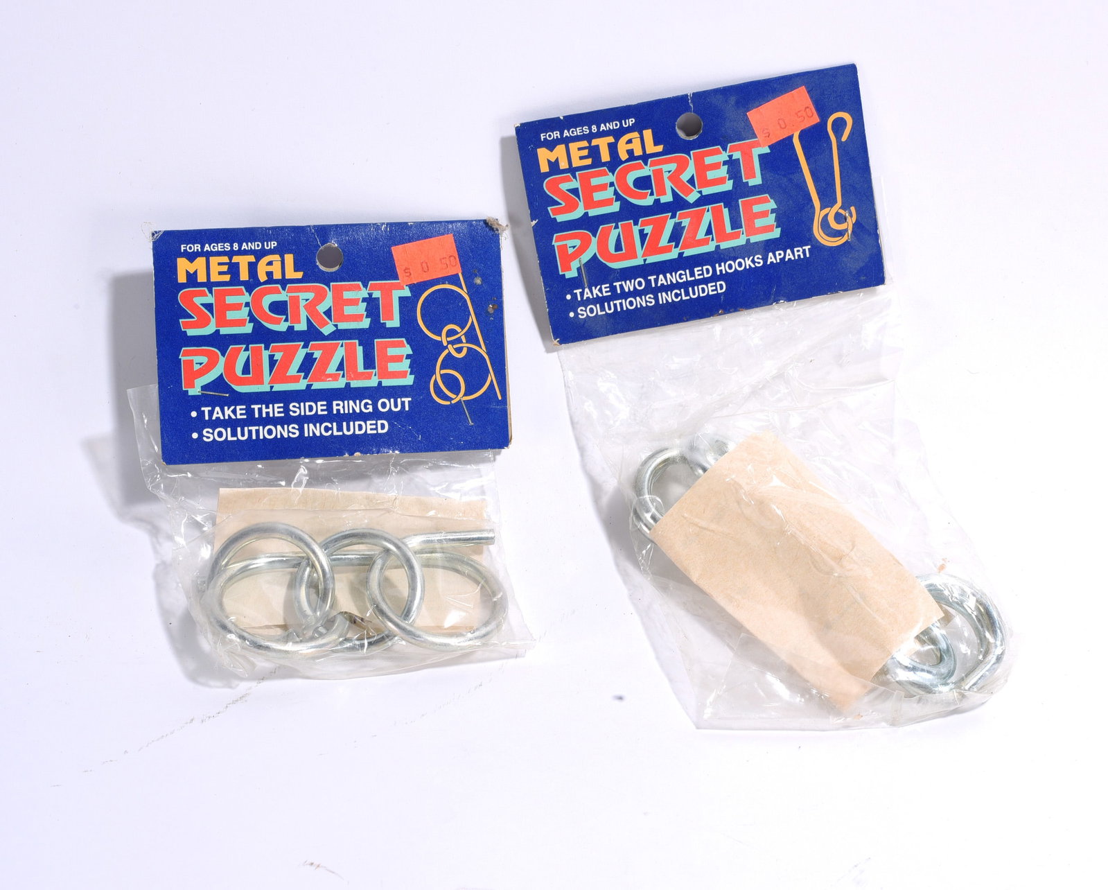 Metal Secret Puzzle Group: Pair of carded Metal Secret Puzzle sets in original packaging. Includes metal disentanglement puzzles with solution instructions. Unopened old store stock examples.