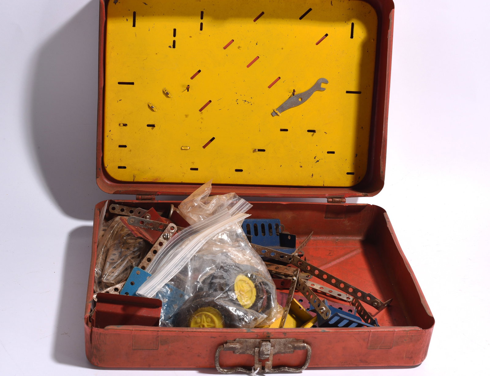 Erector Set Parts in Metal Toolbox: Metal toolbox containing assorted Erector Set parts, wheels, brackets, girders, and construction components. Mixed vintage pieces with wear from use.