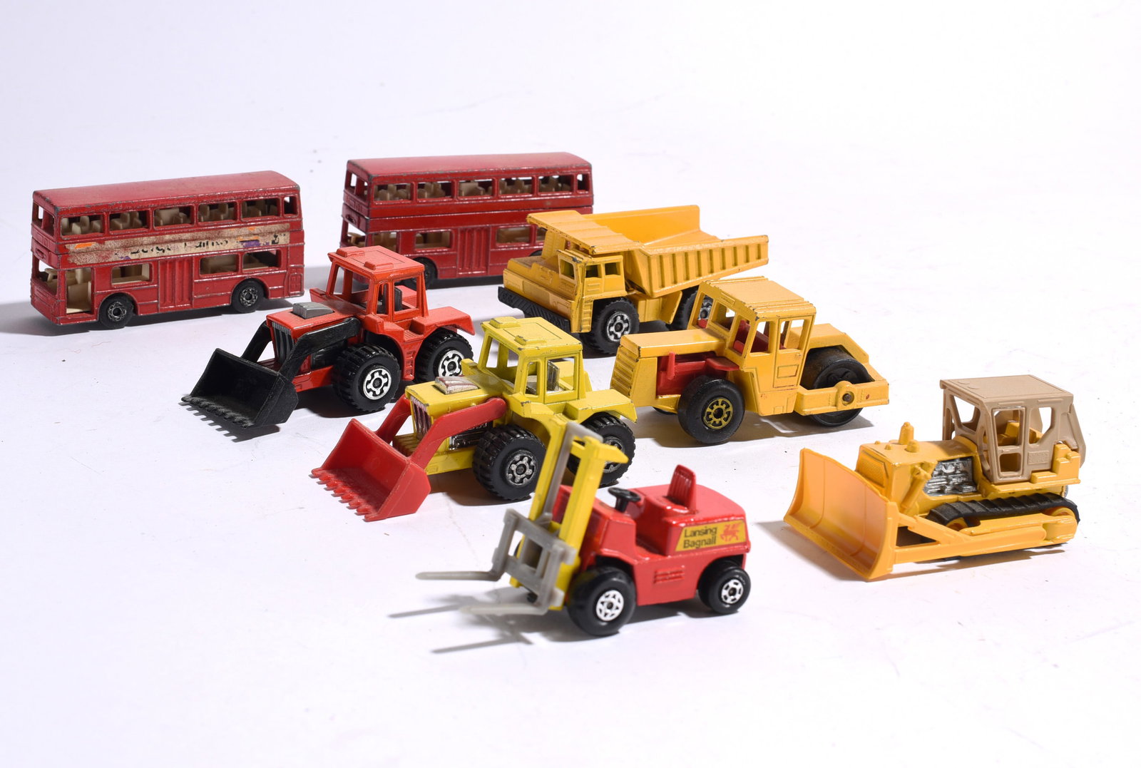 Assorted Construction Vehicles and Double-Decker Buses: Group of die-cast construction vehicles and transportation toys including bulldozers, loaders, dump trucks, forklift, road roller, and two double-decker buses. Showing light to moderate play wear.
