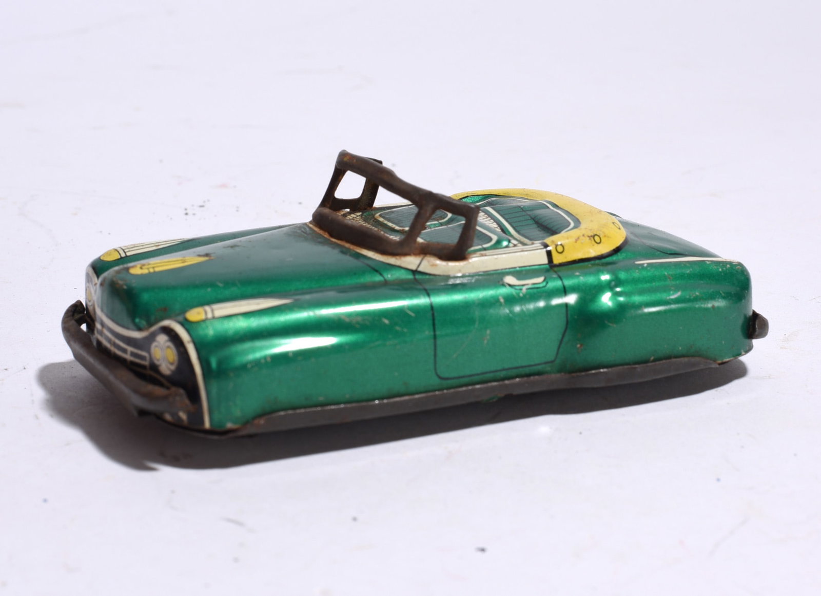 Lithographed Tin Convertible Automobile: Vintage lithographed tin convertible automobile in metallic green finish with printed interior details and windshield frame. Showing age-related wear and surface marks.