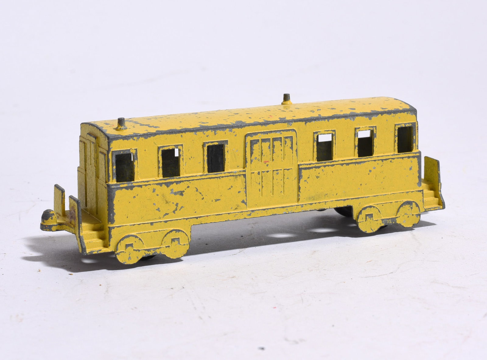 Yellow Toy Passenger Coach: Early painted metal passenger coach railcar in yellow finish with black trim. Wear, paint loss, and oxidation present throughout.