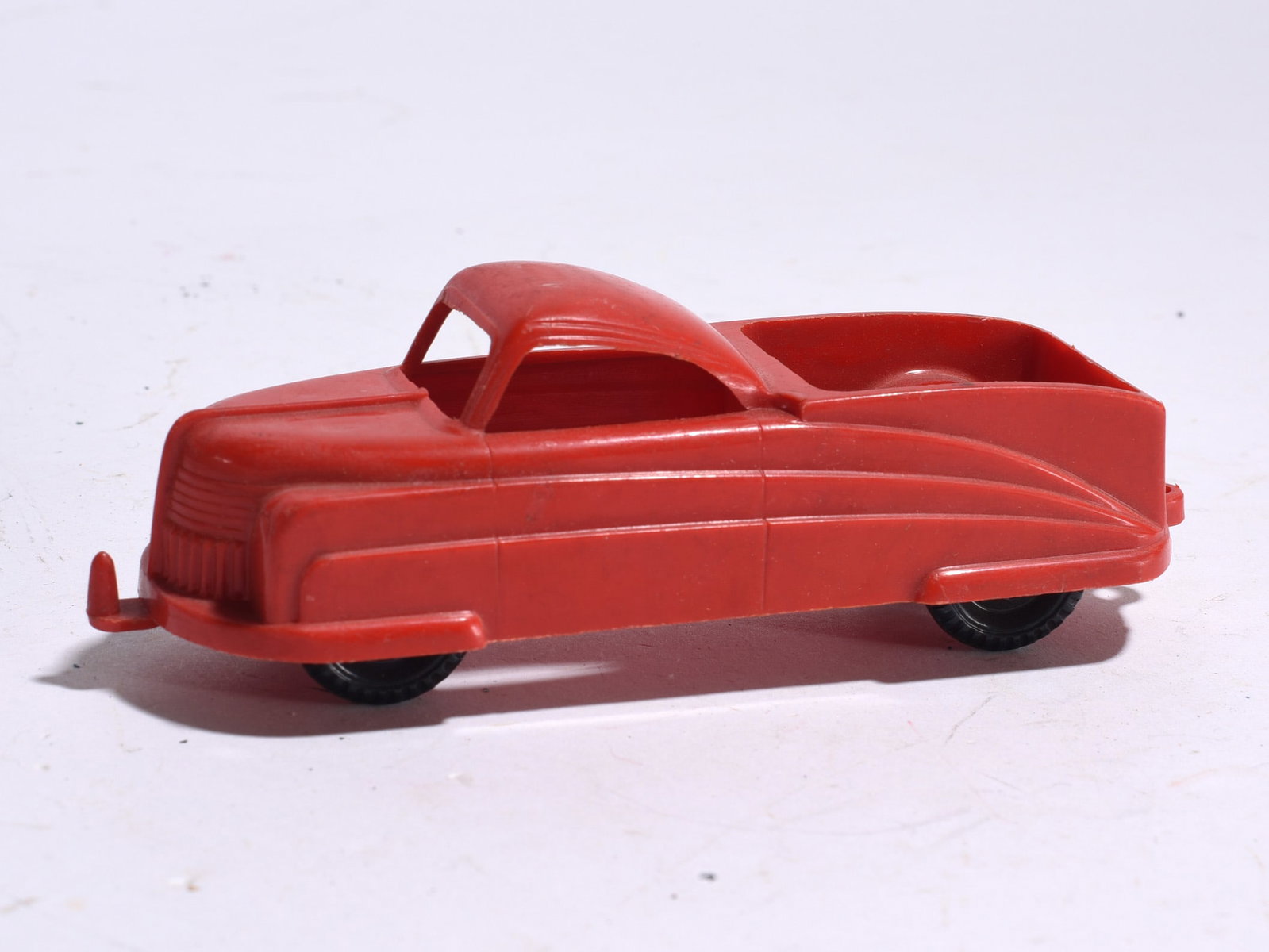 Streamlined Plastic Pickup Truck: Streamlined red plastic pickup truck with enclosed cab and cargo bed. Features Art Deco-inspired body lines and original wheels.