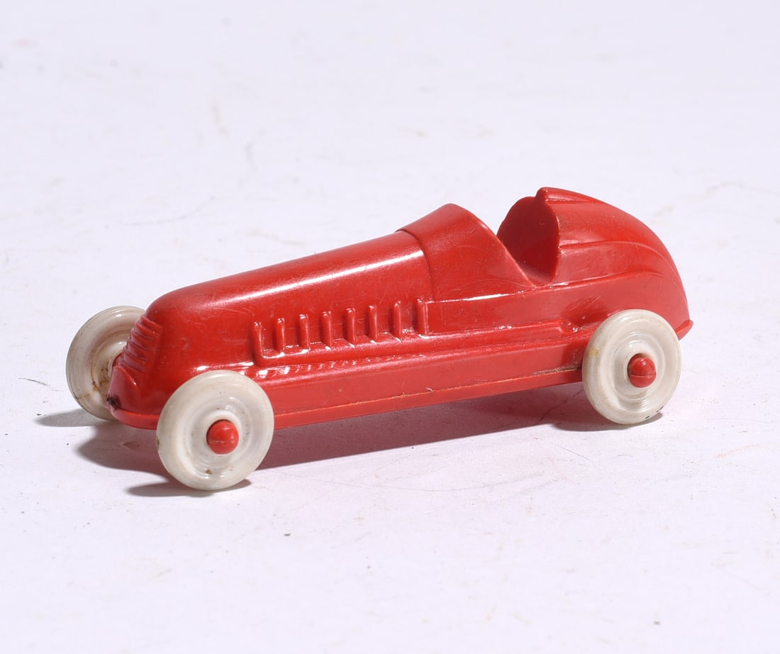 Plastic Racing Car: Red molded plastic racing car with open cockpit and white wheels. Simple streamlined design with light wear from handling.