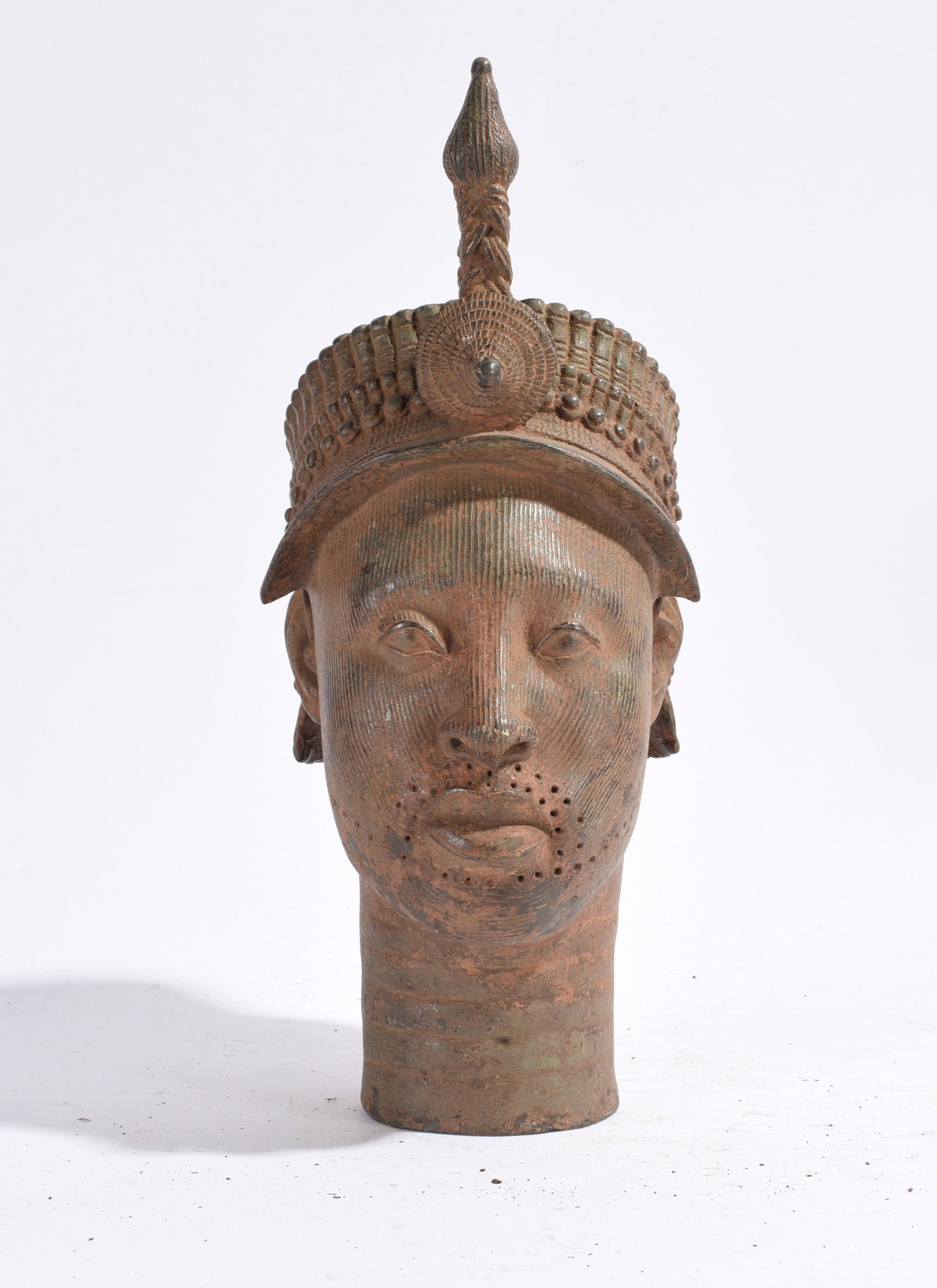 Benin Style Bronze Royal Head with Crown: Cast bronze royal head in the Benin tradition featuring an elaborate crown, facial scarification, and finely incised linear decoration. Displays an attractive aged patina with evidence of age and hand