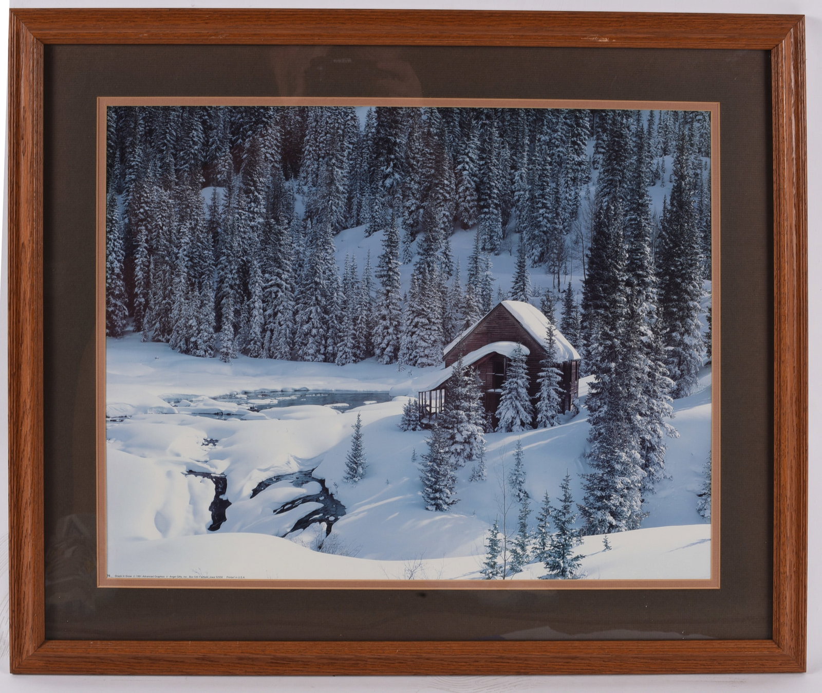 Winter Cabin in Snow Framed Color Landscape Print: 27"X23" Color landscape print featuring a snow-covered cabin nestled among towering evergreen trees beside a winding creek. Matted in a dark brown mat with a wood frame, creating a striking winter sce