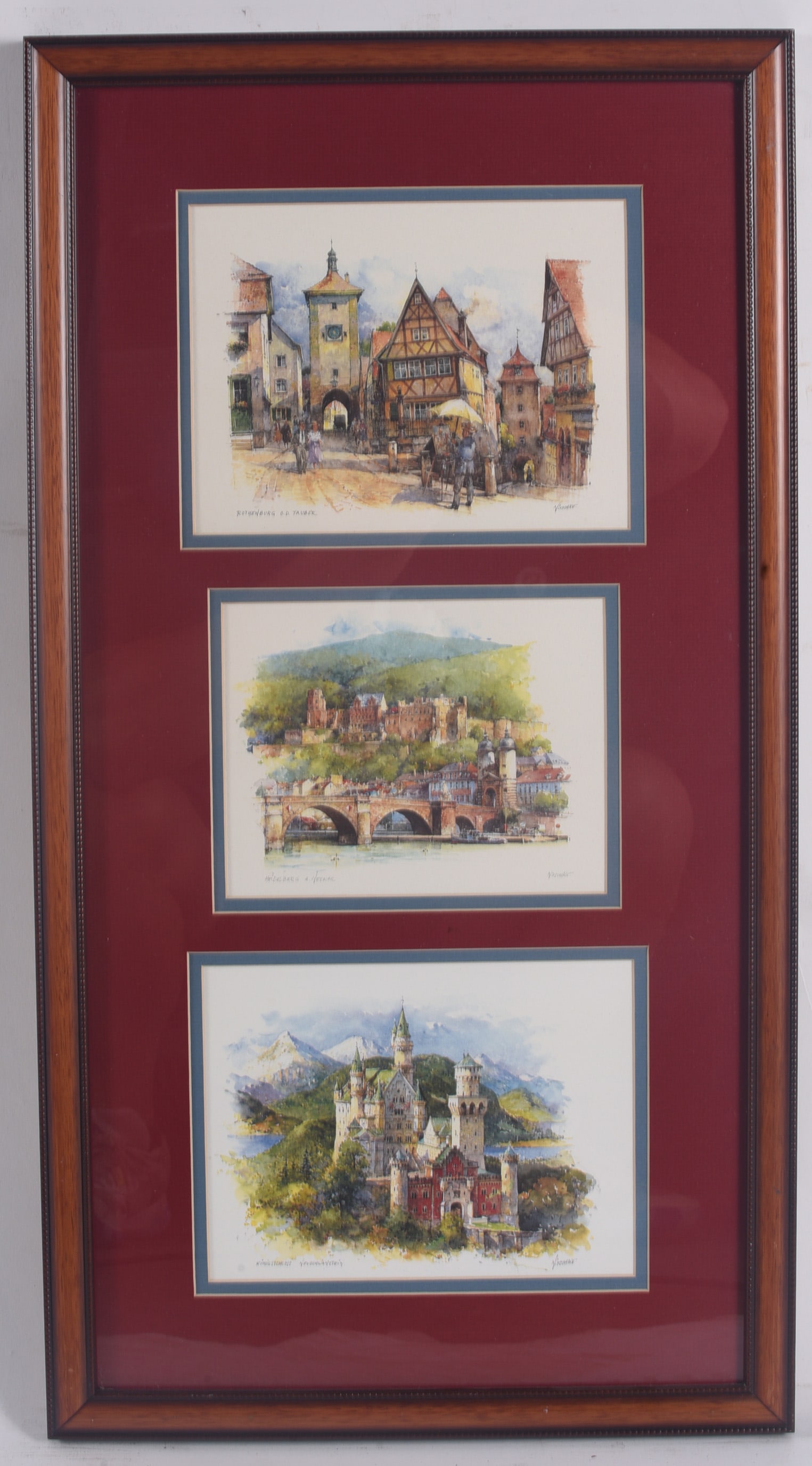 Framed European Landmark Watercolor Print Collection: 14"x26" Triple-opening framed display featuring watercolor views of Rothenburg ob der Tauber, Heidelberg, and Neuschwanstein Castle. Double matted in burgundy and blue accents and housed in a wood fra