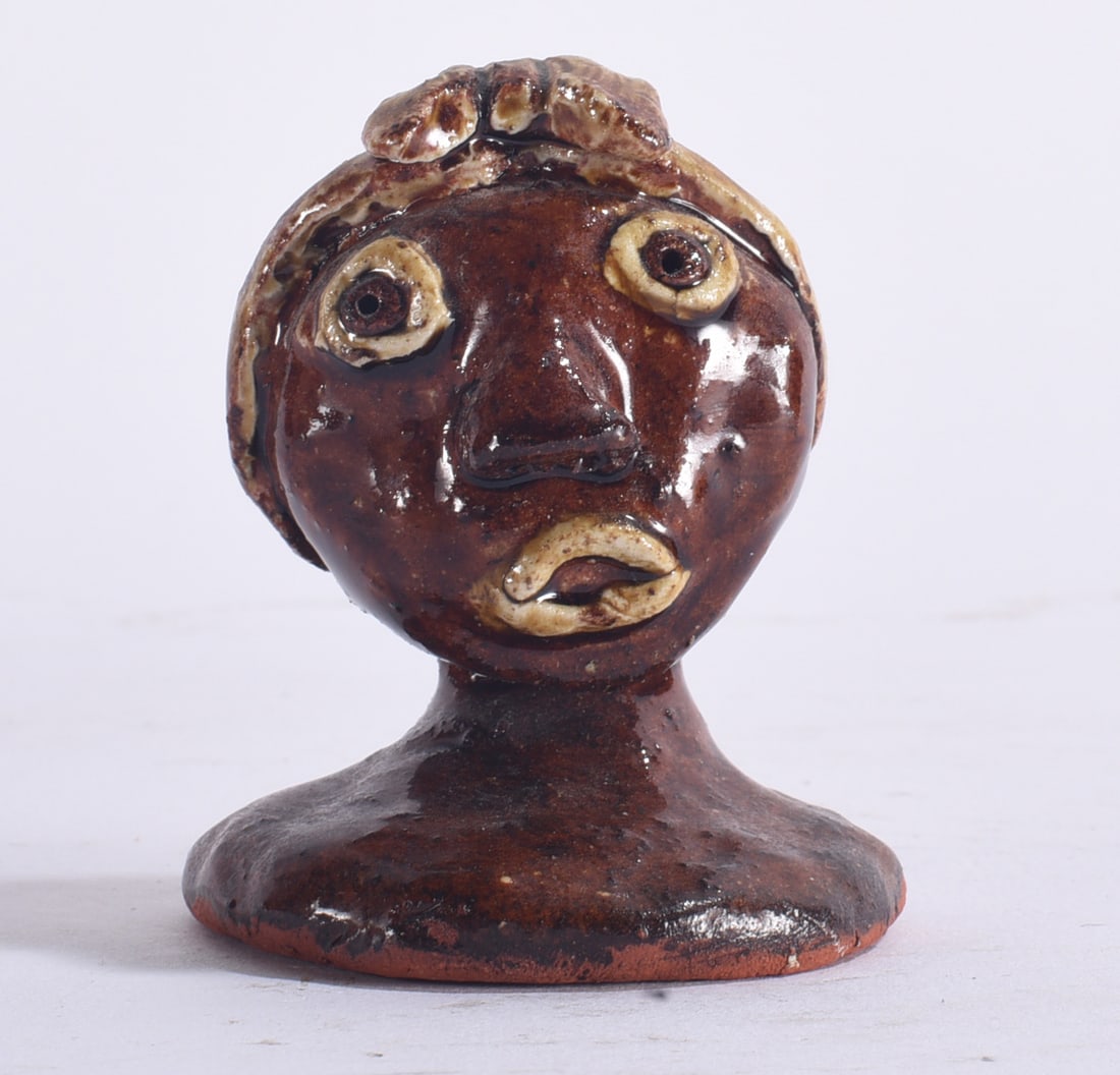 Peggy Hodge Folk Pottery Small Bust: 3" Small folk pottery bust with warm brown glaze, exaggerated applied eyes, nose and lips, and contrasting cream-colored facial and hair details.