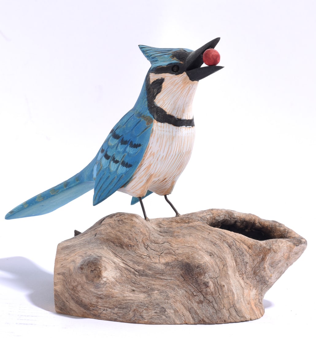 Eugene Ownby Folk Art Bird Carving: 6" Eugene Ownby is an American folk carver known for finely observed and whimsical carved birds. This painted wood carving depicts a blue jay holding a red berry in its open beak, mounted on a natural