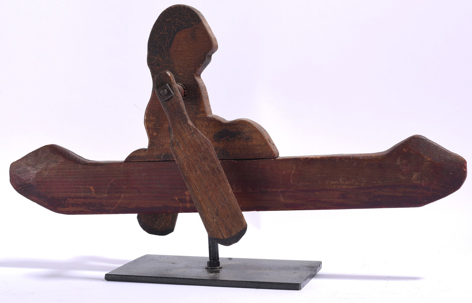 Native American Carved Canoe Whirligig: 17"x10" Wooden Native American canoe whirligig featuring a seated figure with articulated paddle and simple hand-cut construction. Mounted on a later metal display stand, the piece retains a dark, wea