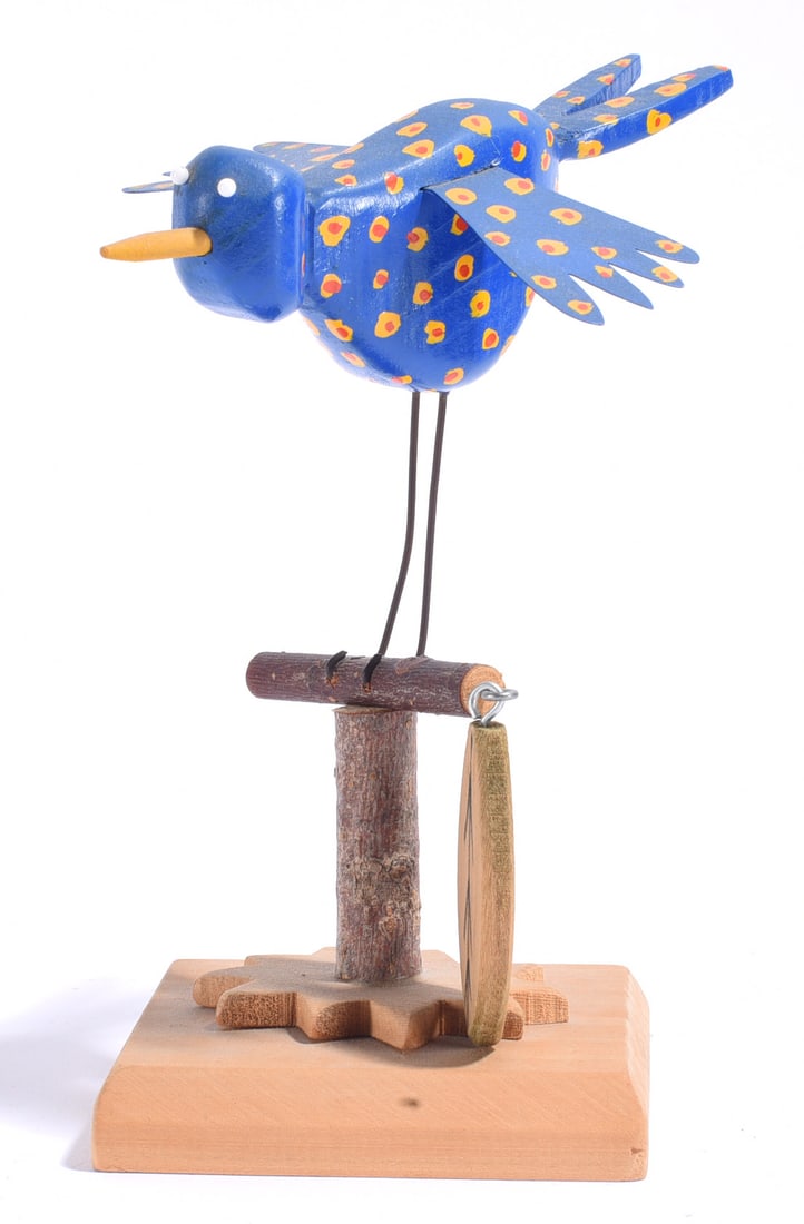 Carved Bird Signed Carey: 8" Whimsical carved and painted folk art bird signed Carey, featuring a bright blue body decorated with yellow and orange spots, outstretched wings, applied eyes and long metal legs. The bird is perch